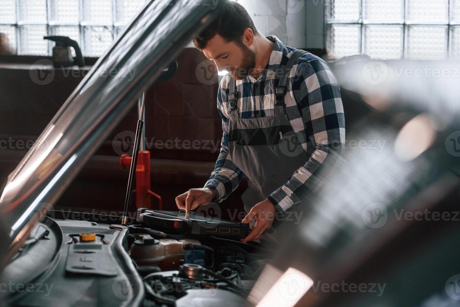 Hood ,,of the car is opened. Using tablet. Man in uniform is working in the auto salon photo