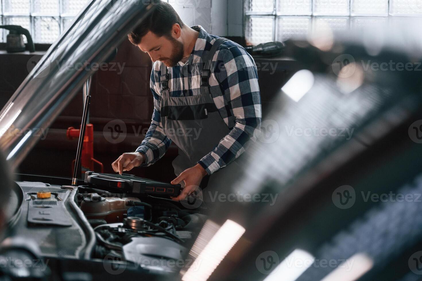 Hood of, the, car is opened. Using tablet. Man in uniform is working in the auto salon photo
