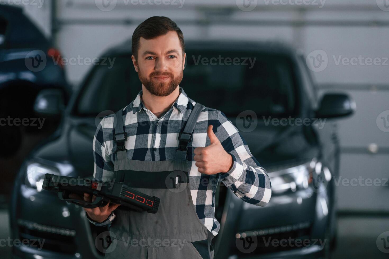 Showing gesture and smiling. Holding tablet. Man in uniform is working in the auto salon photo