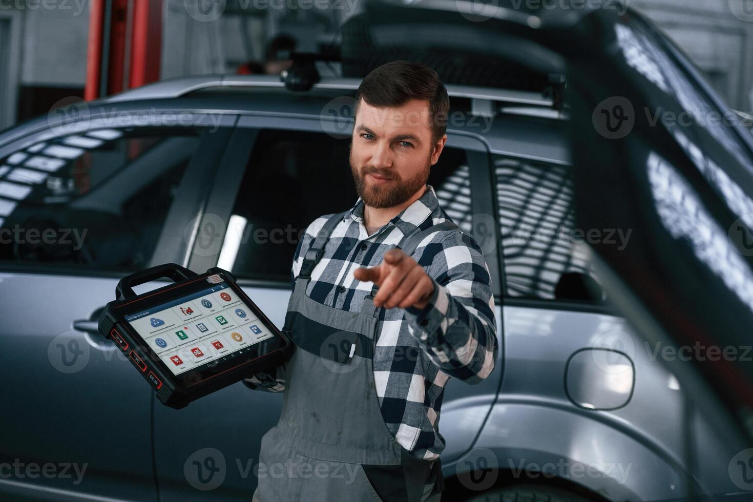 Showing gesture,and smiling. Holding tablet. Man in uniform is working in the auto salon photo