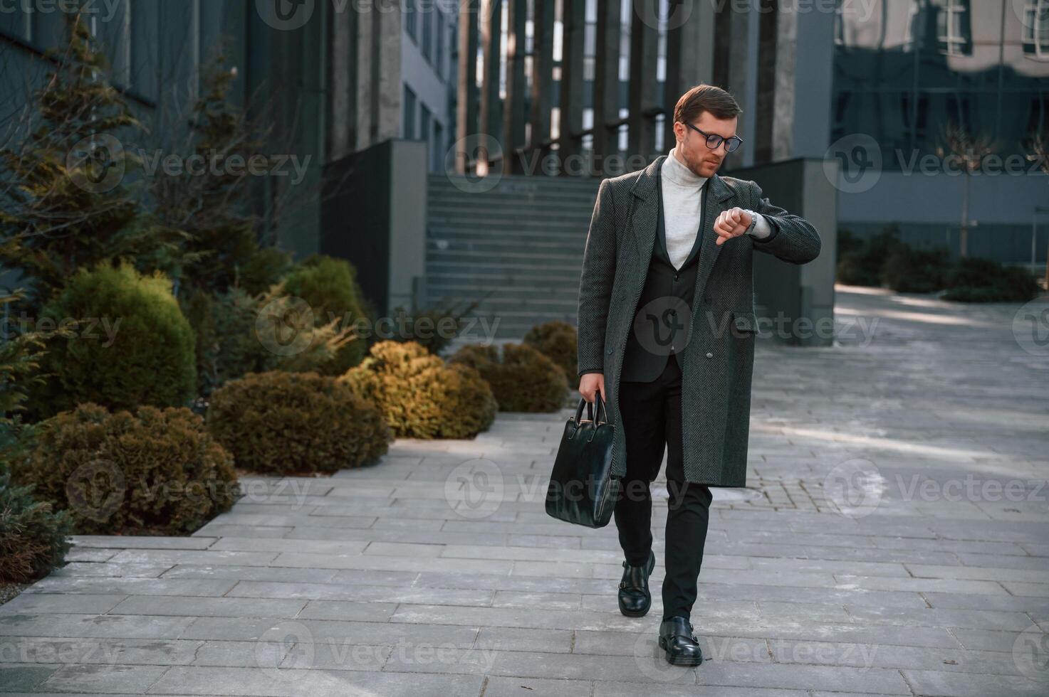 Checking the time. Handsome man in formal clothes is outdoor near the business building photo