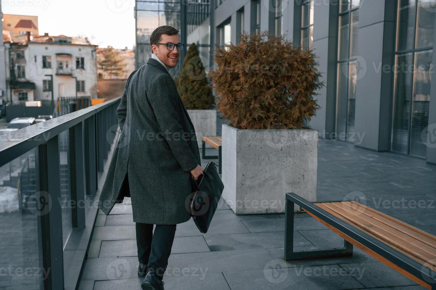 Holding the bag. Handsome man in formal clothes is outdoor near the business building photo