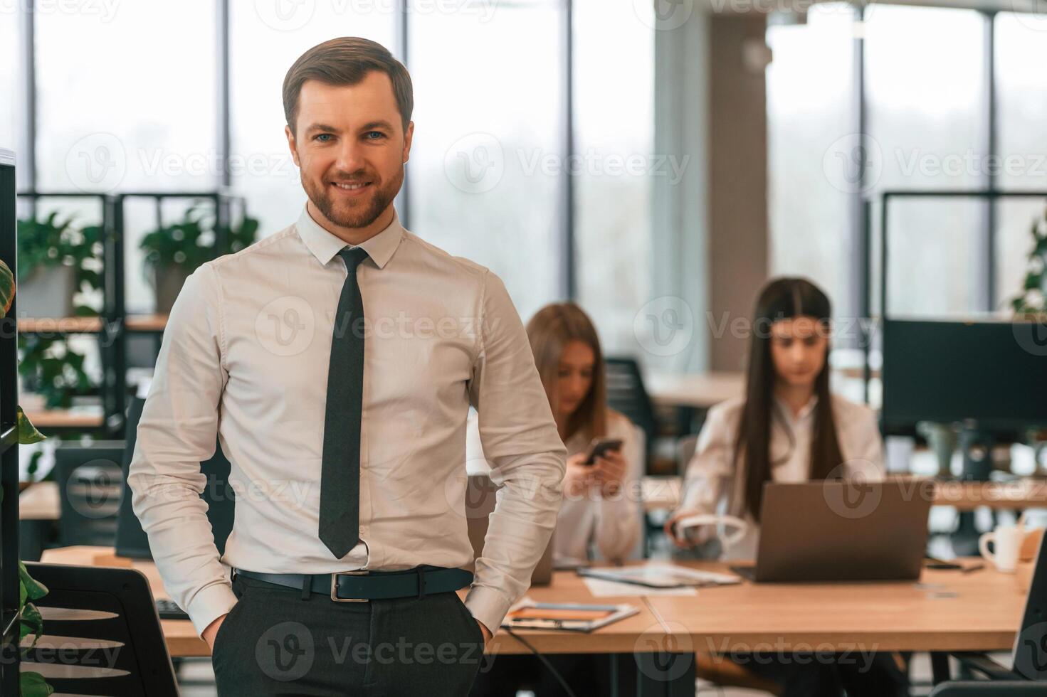 Man in tie is standing in front ,of his colleagues. Business people in formal clothes are working in the office together photo