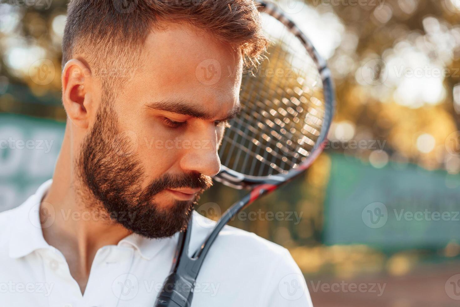 Standing, with racket in hands. Young man is on the tennis court at sunny daytime photo