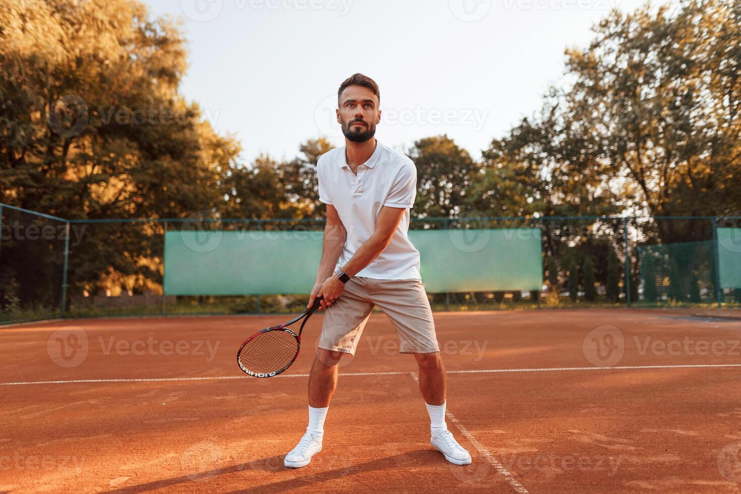 Active training. Young man, is on the tennis court at sunny daytime photo