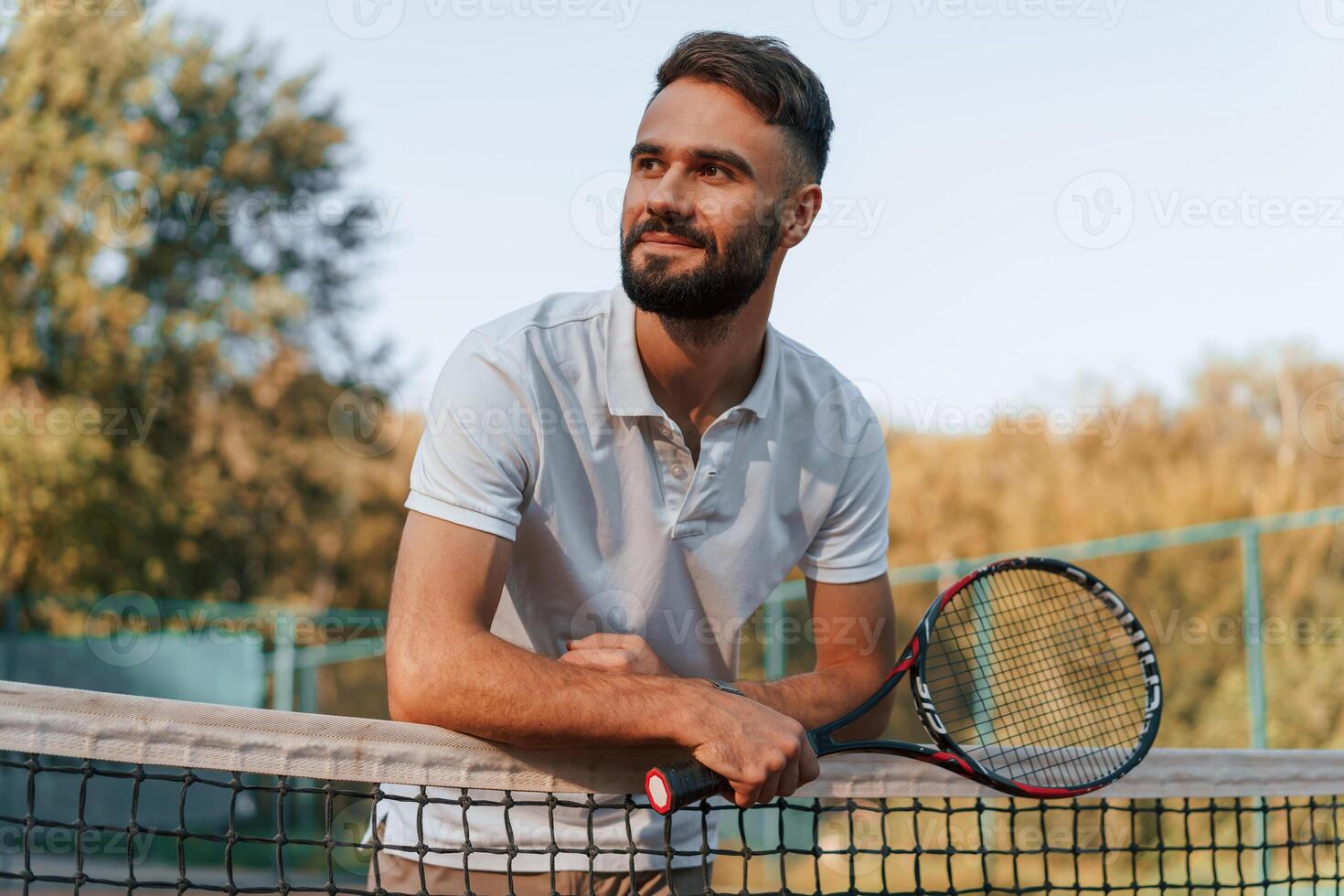 Standing with ,racket in hands. Young man is on the tennis court at sunny daytime photo