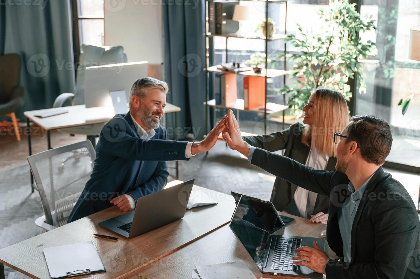 Making high, five, sitting by ,the table. Group of business people are working in the modern office photo