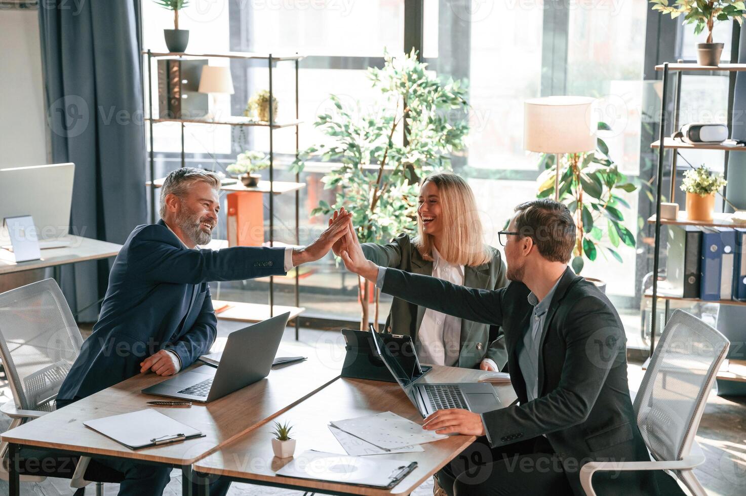 Making high five,, sitting by the table. Group of business people are working in the modern office photo