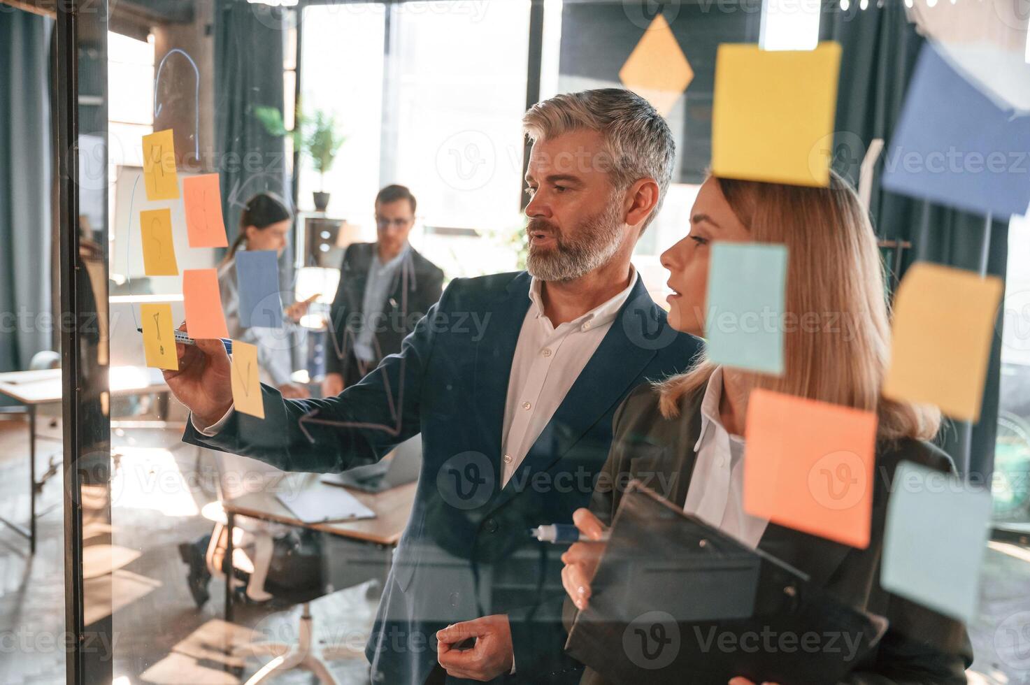 Company growth. Many stickers on the glass. Group of business people are working in the modern office photo