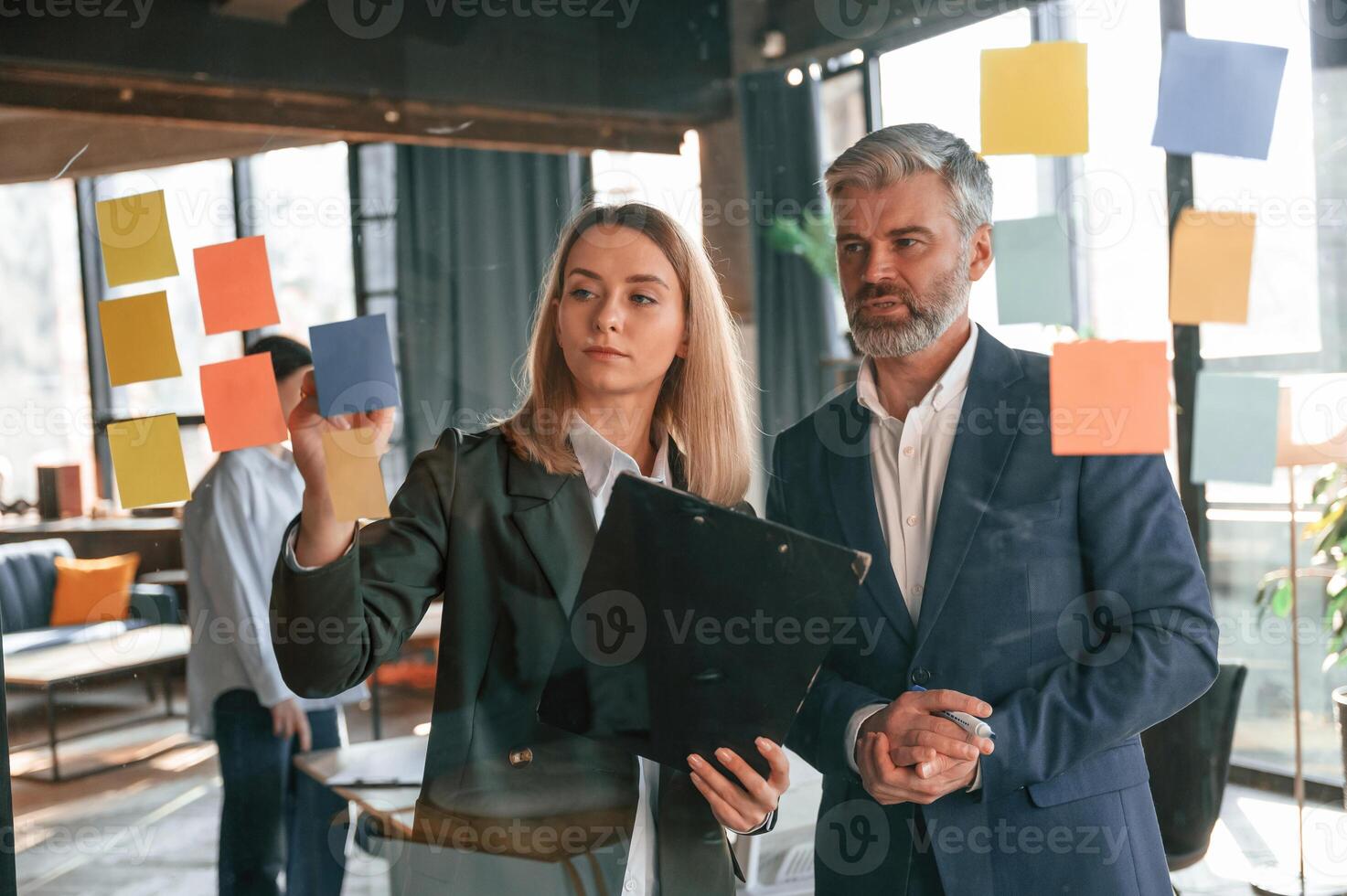 View ,through ,the, glass full of stickers. Man and woman are standing. Group of business people are working in the modern office photo