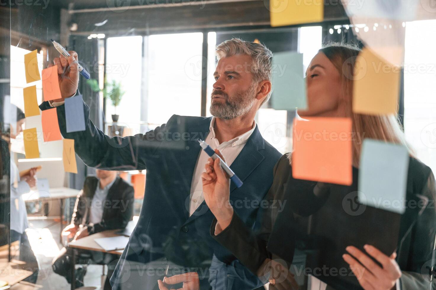 View ,through the glass full of stickers. Man and woman are standing. Group of business people are working in the modern office photo