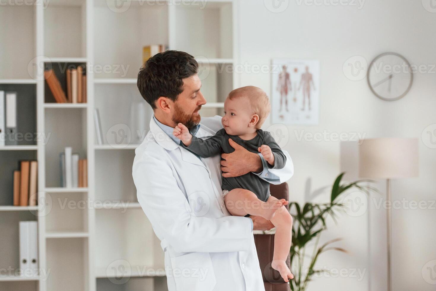 Standing, and holding boy. Doctor, with little baby is working in the cabinet photo