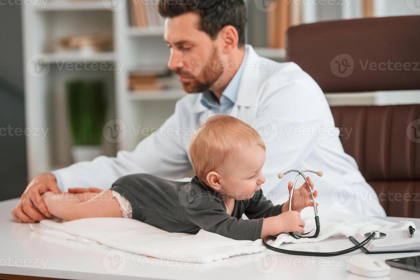 With stethoscope.. Doctor with little baby is working in the cabinet photo