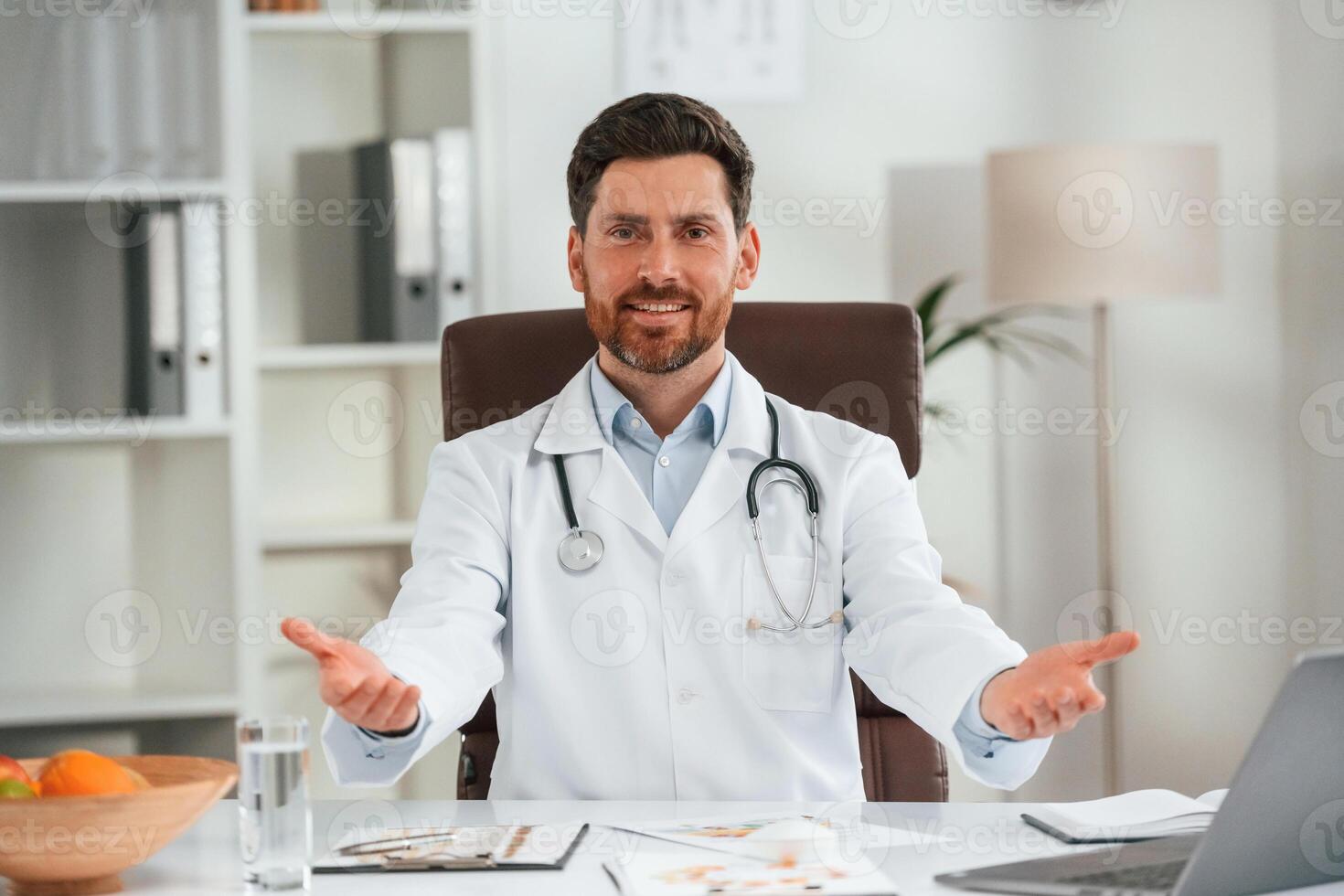 In white coat, sitting.. Doctor in formal clothes is working in the cabinet photo