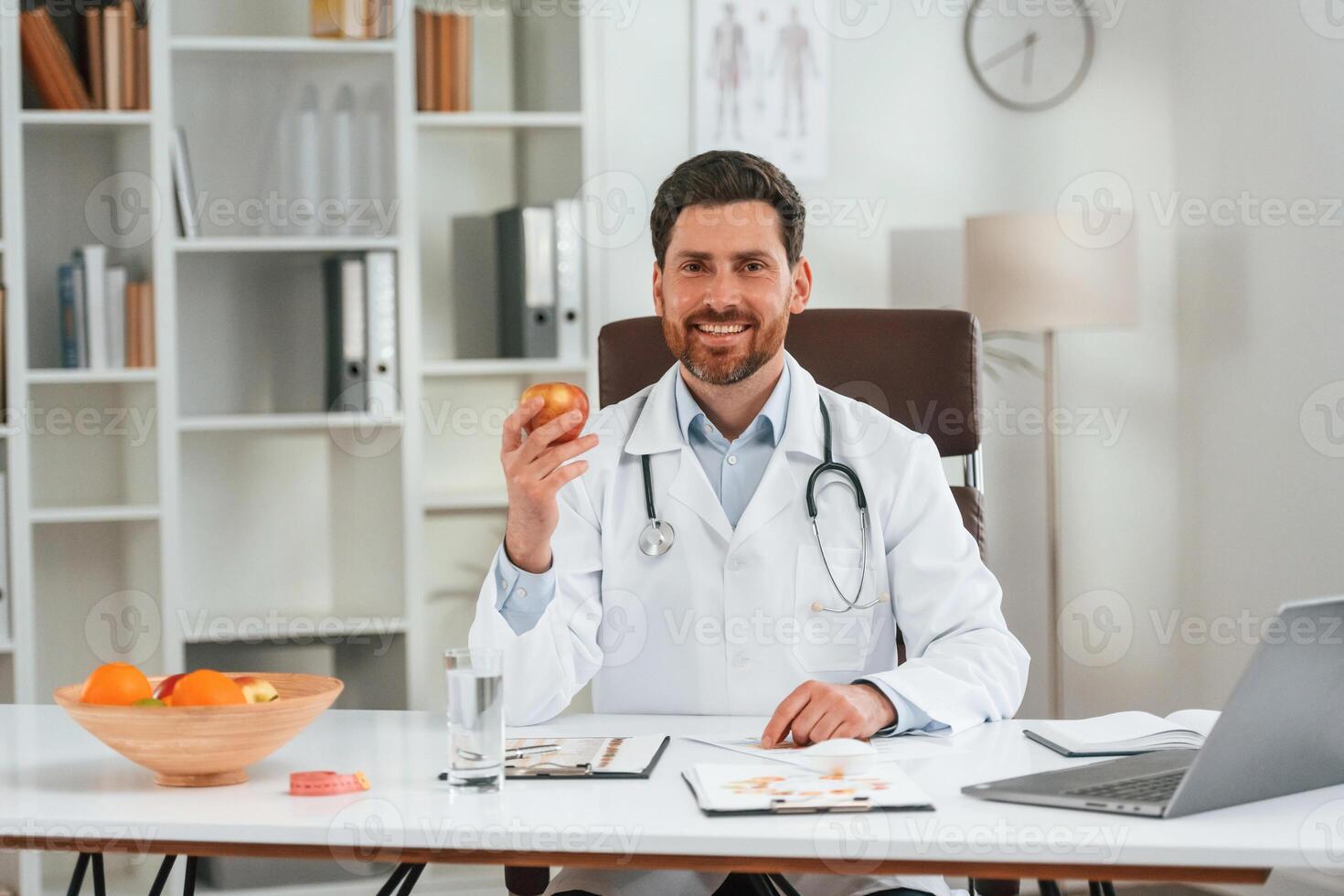 Holding an apple.. Doctor in formal clothes is working in the cabinet photo