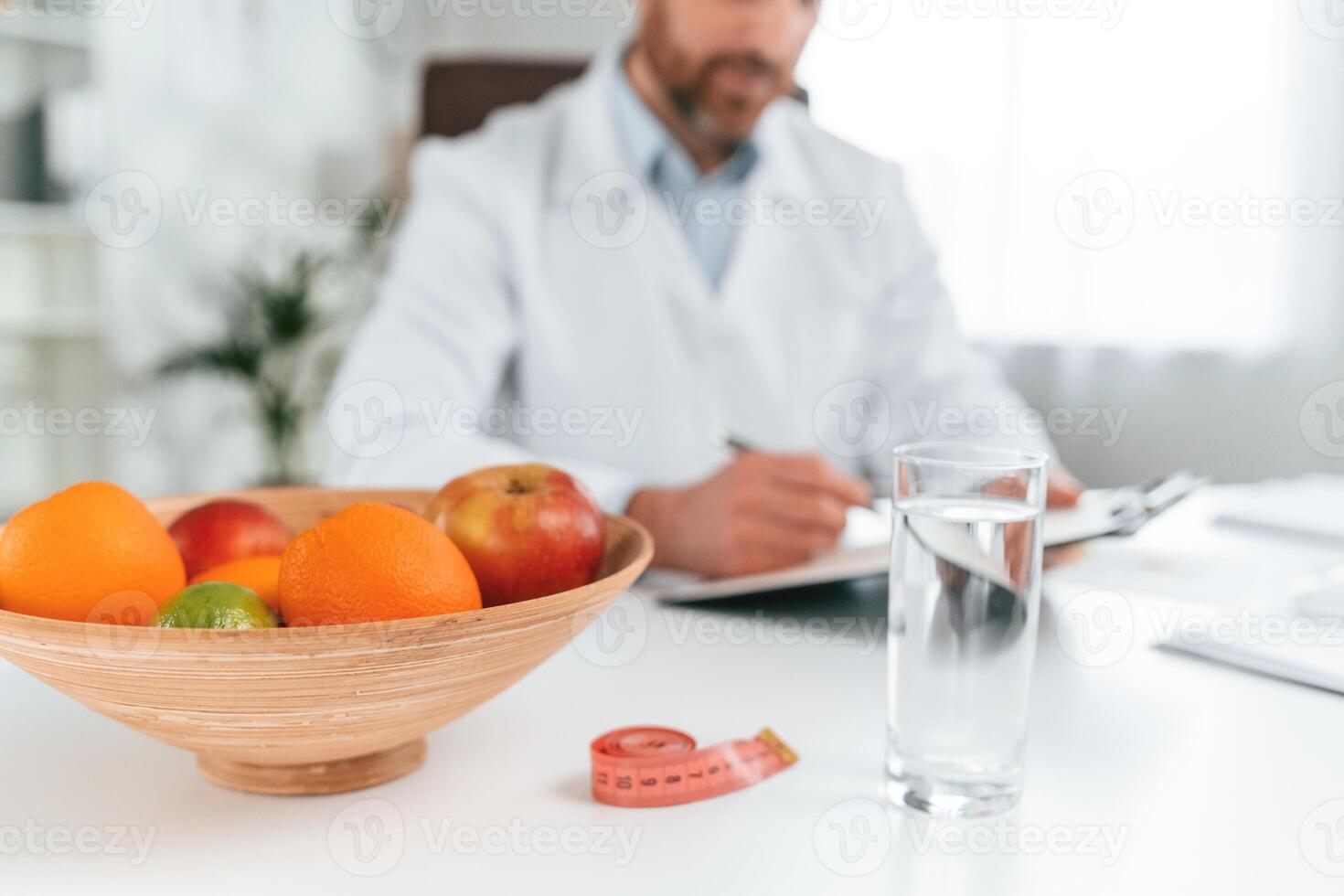 Fruits is on the table. Doctor in formal clothes is working in the cabinet photo
