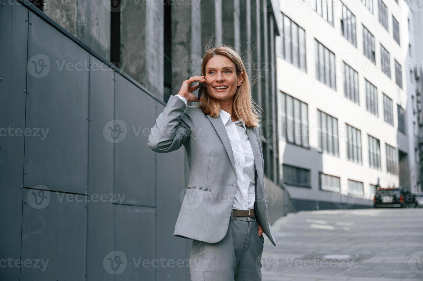Conversation by the phone. Woman in formal, clothes is outdoors near the business building photo