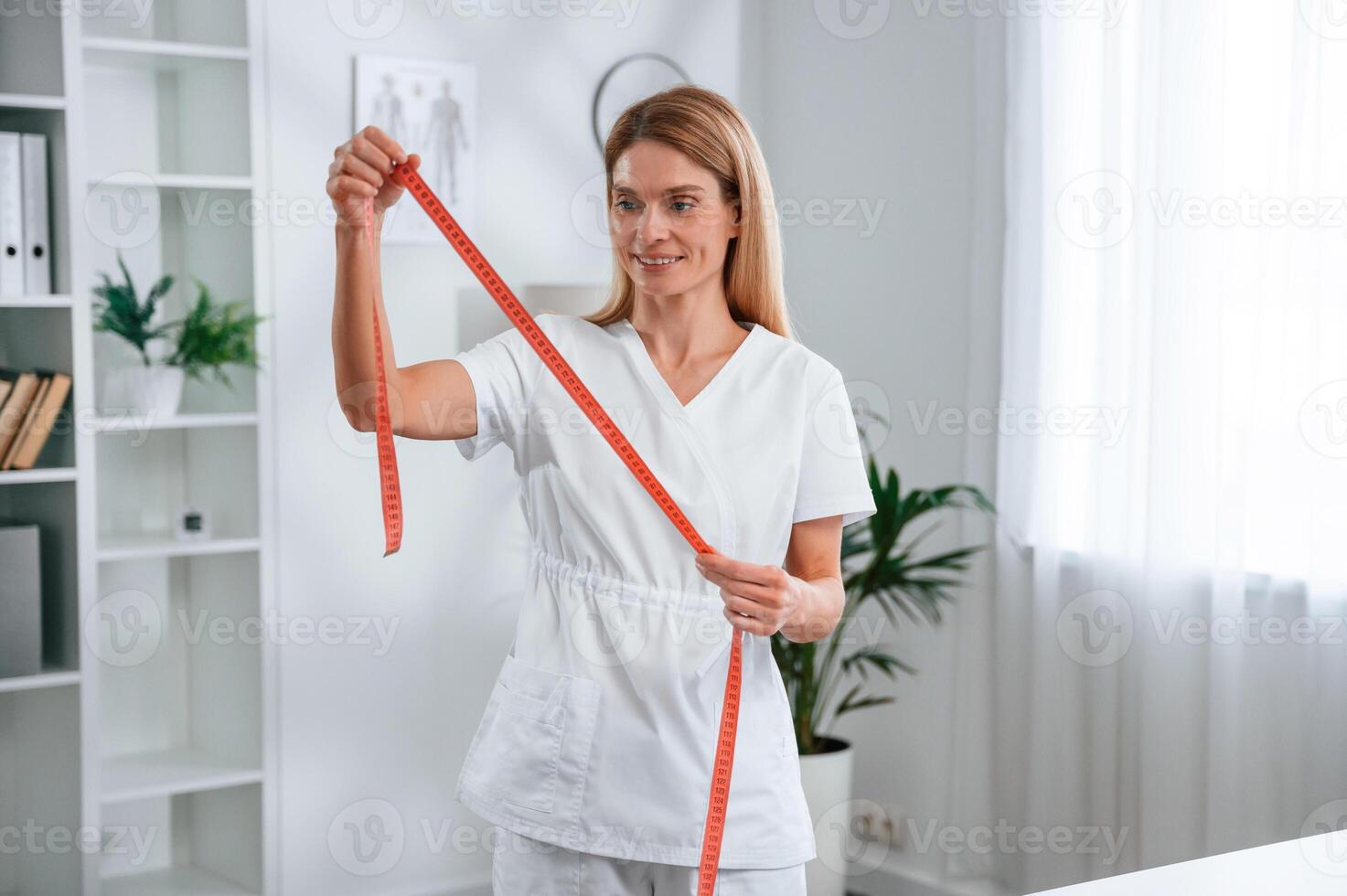 With measuring ,tape ,in hands, conception of diet. Young female doctor in white coat is indoors photo