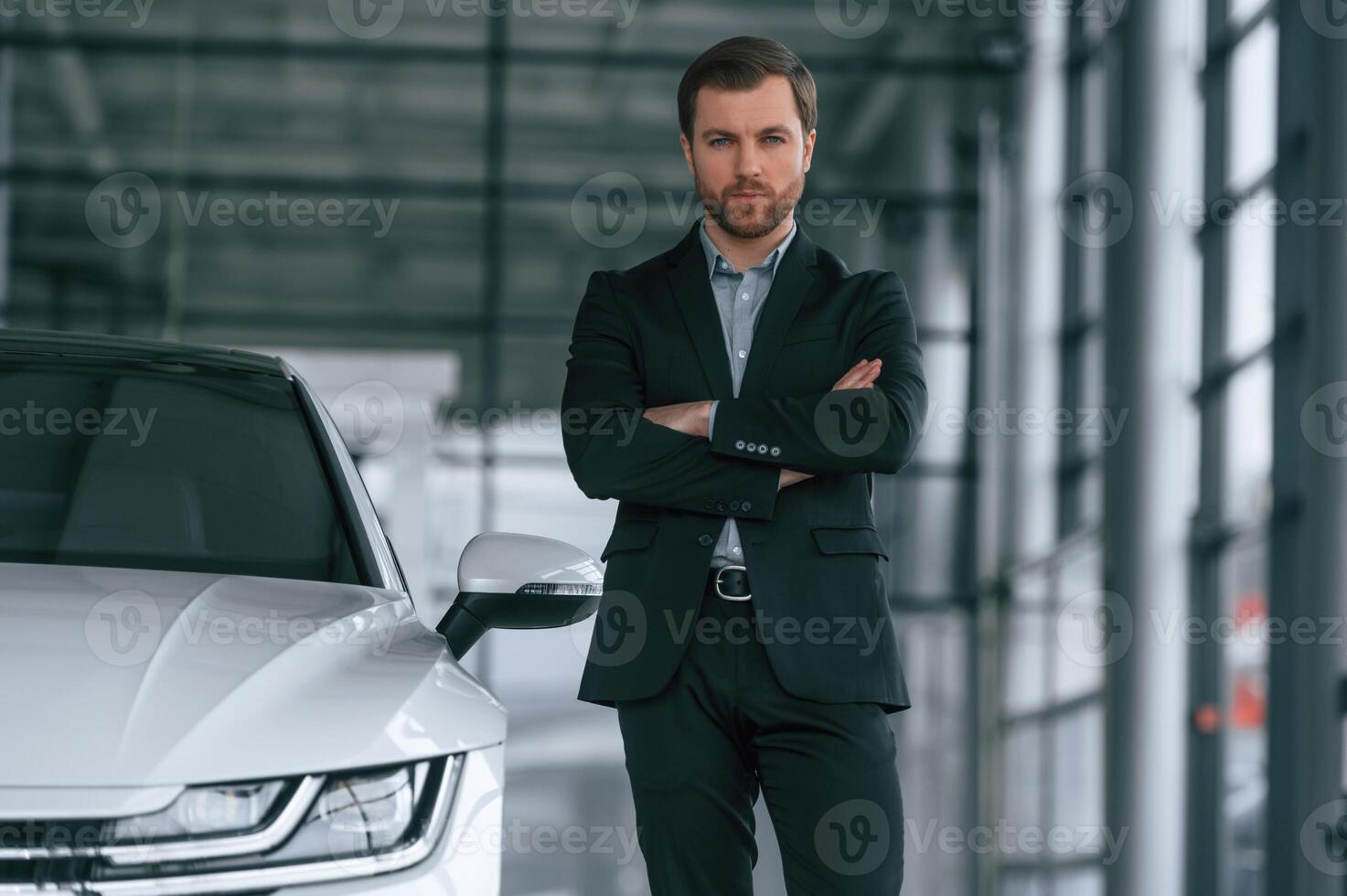 Man ,in black suit is indoors in the car dealership near automobile photo