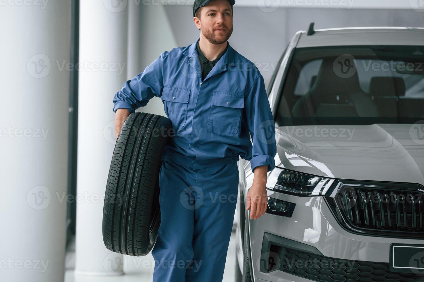 With tire in the hands. .Man in blue uniform is working in the car service photo