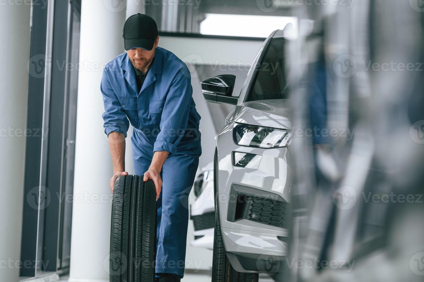 Moving the ,tire. Man in blue uniform is working in the car service photo