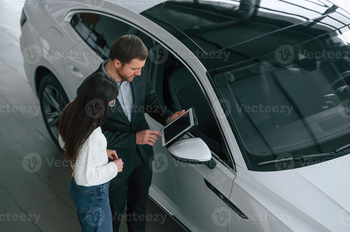 Talking,, holding tablet. Man is showing the new automobile to the woman customer in the car dealership photo