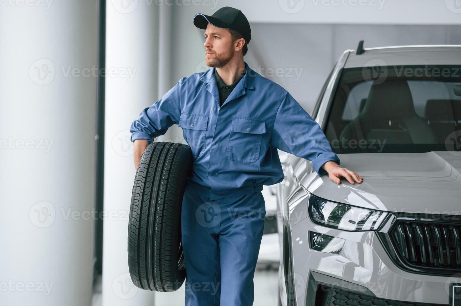 With tire in the hands. Man, in blue uniform is working in the car service photo
