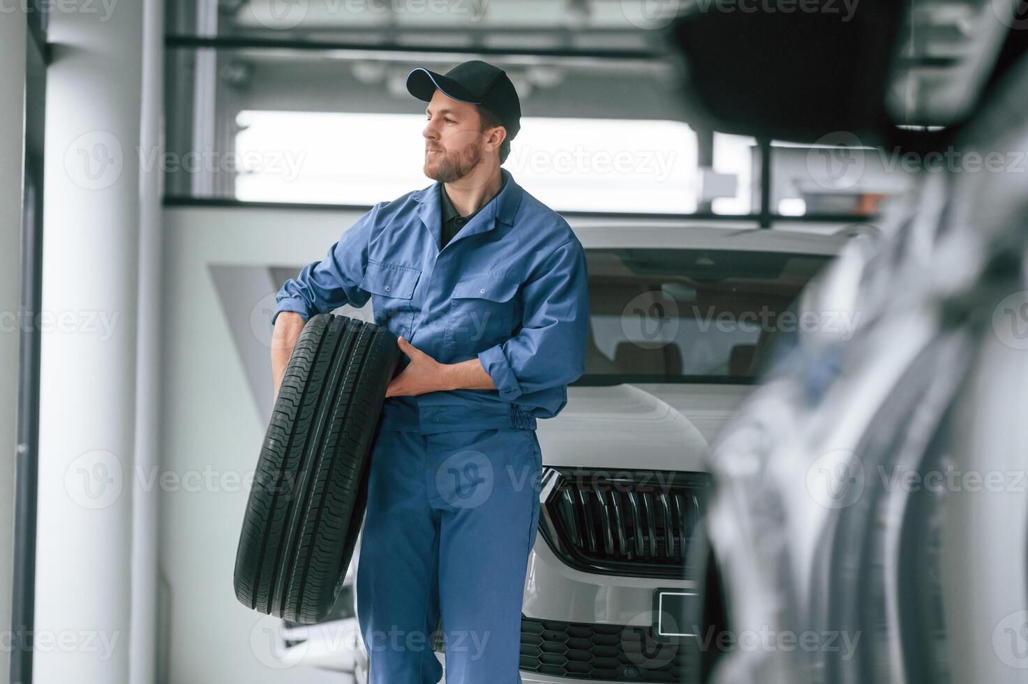 With tire ,in the hands. Man in blue ,uniform is working in the car service photo