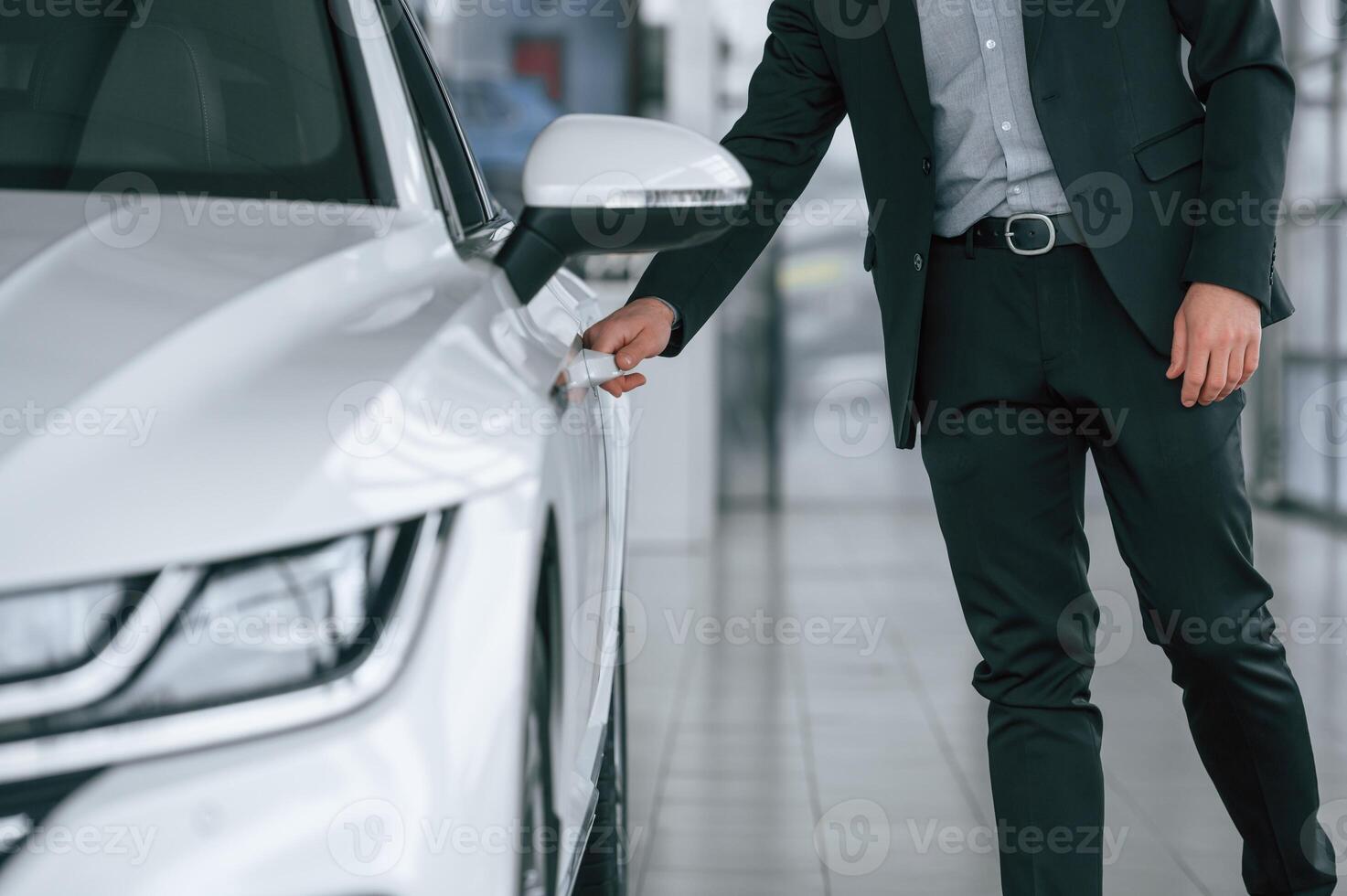 Close up view of man in suit that is opening the door of the new white colored automobile photo