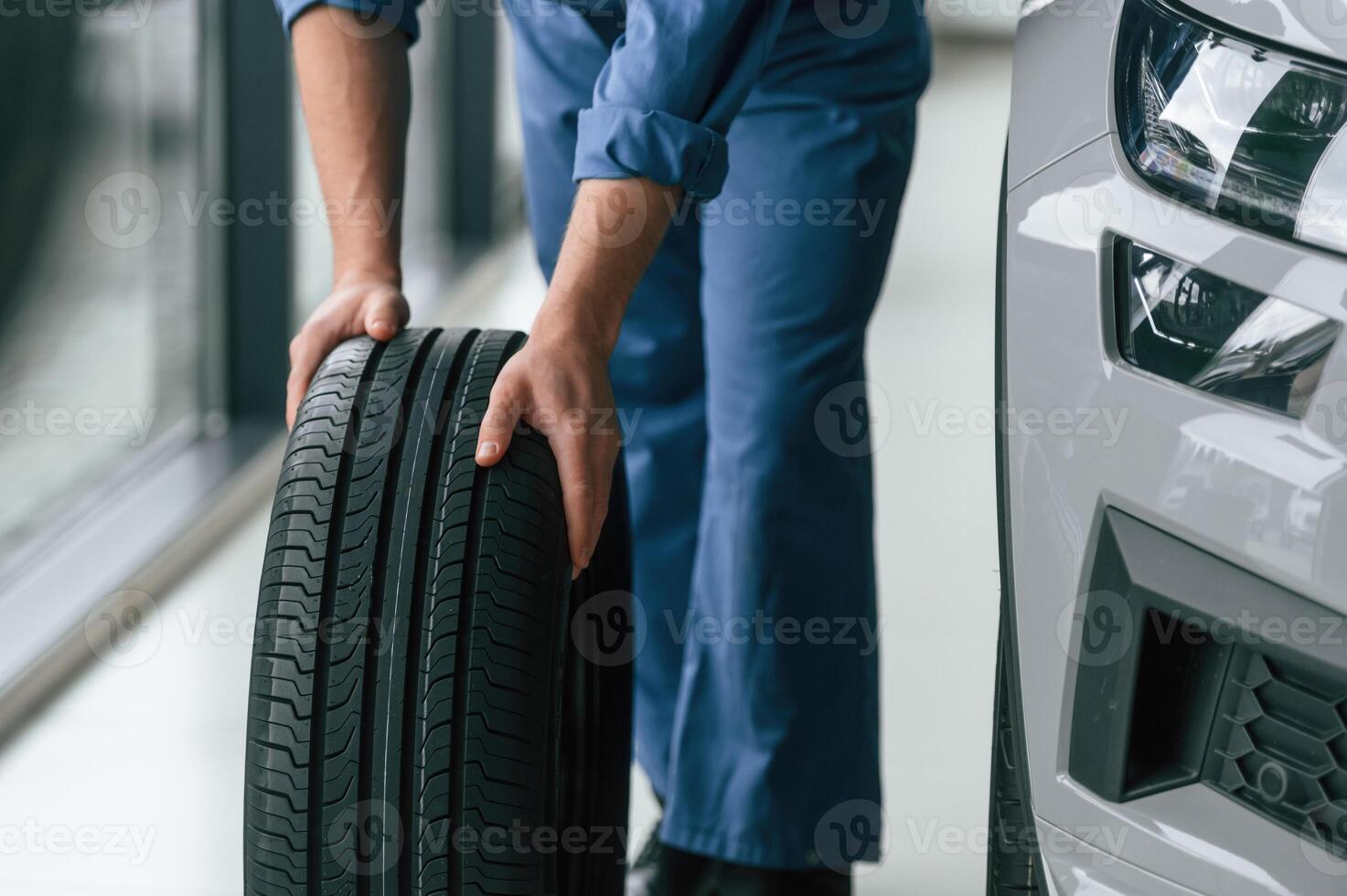 Close up, view. Moving the tire. Man in blue uniform is working in the car service photo
