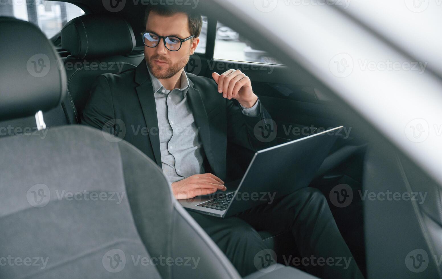 With ,laptop, working. Man in formal business clothes is sitting in the modern automobile photo
