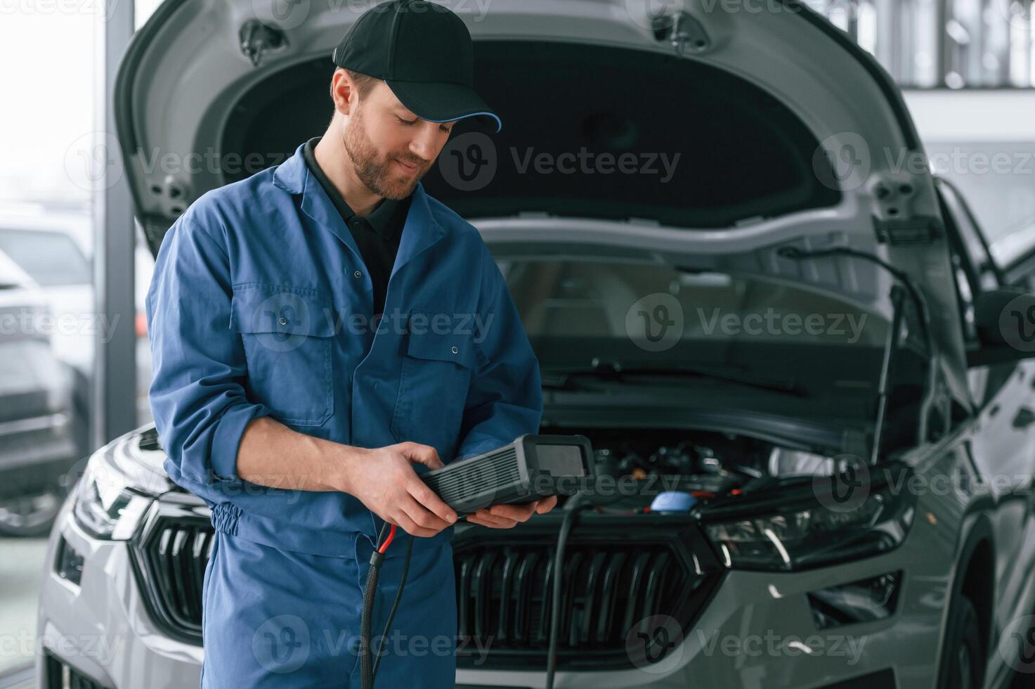 Holding electricity measuring, tool. Man in blue uniform is working in the car service photo