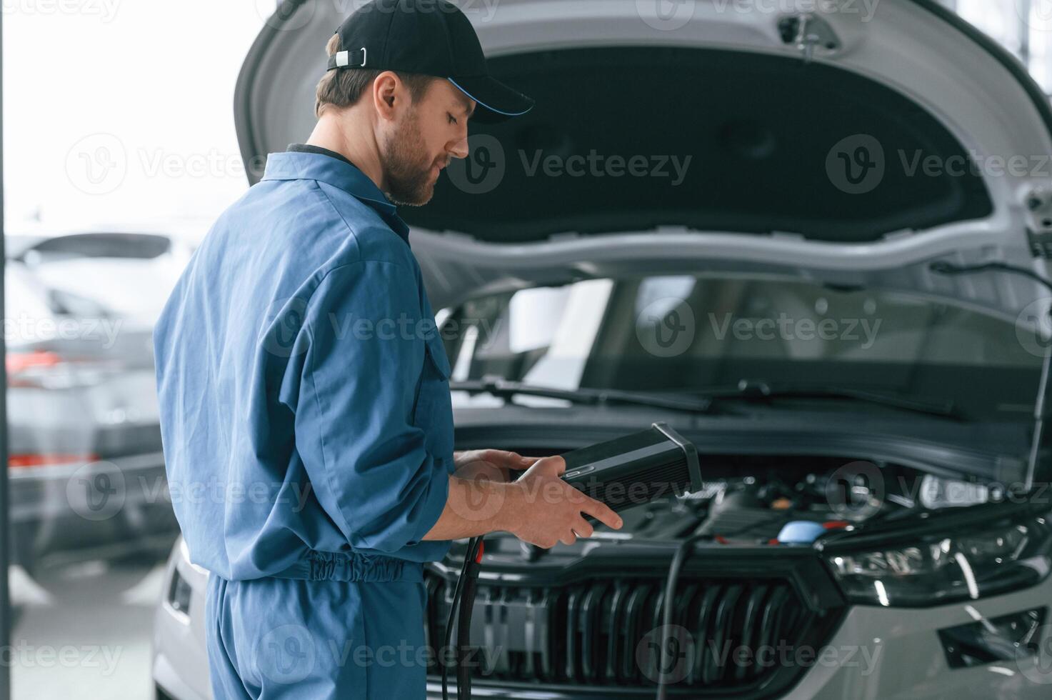 Holding, electricity measuring tool. Man in blue uniform is working in the car service photo