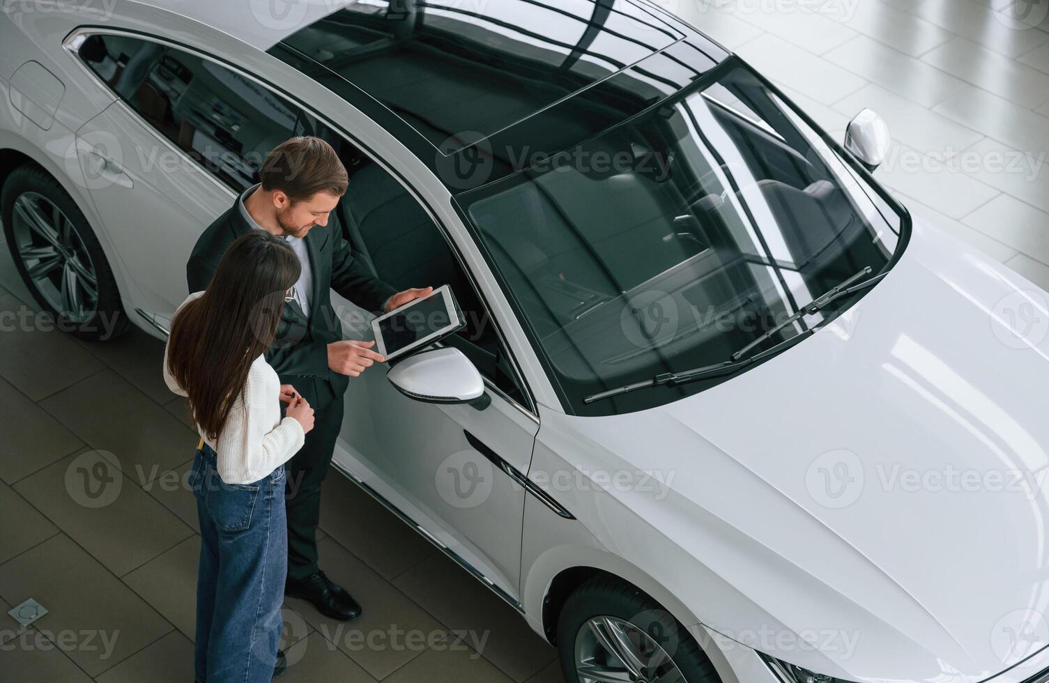Man is ,showing the new automobile to the woman customer in the car dealership photo