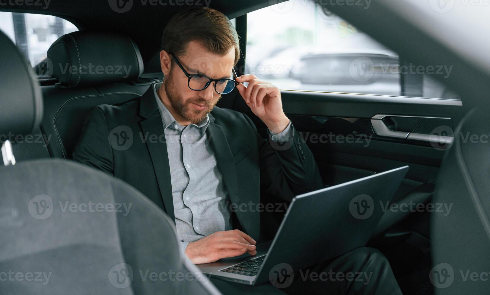 With laptop, working... Man in formal business clothes is sitting in the modern automobile photo