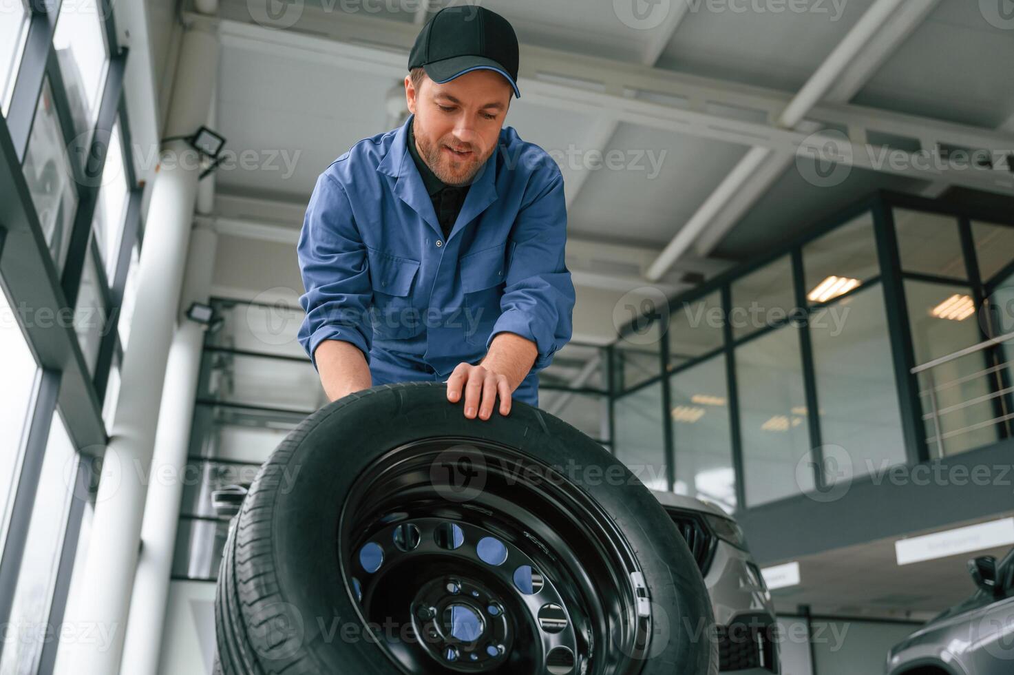 Front view, moving the, tire. Man ,in blue uniform is working in the car service photo