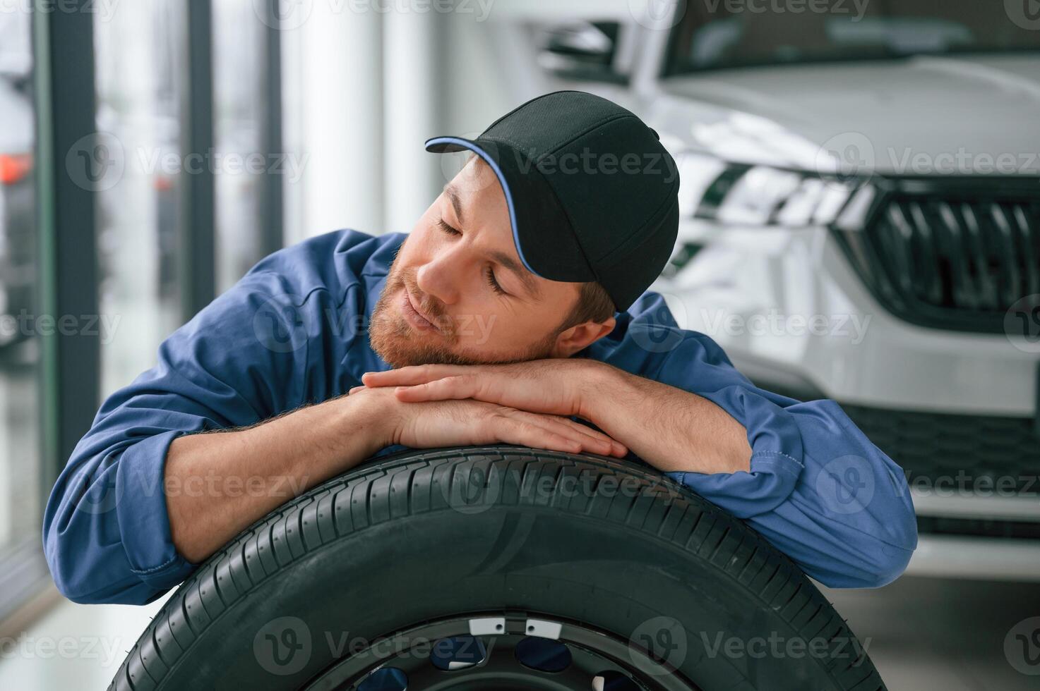 New tire. Leaning on it. Man, in blue ,uniform is working in the car service photo