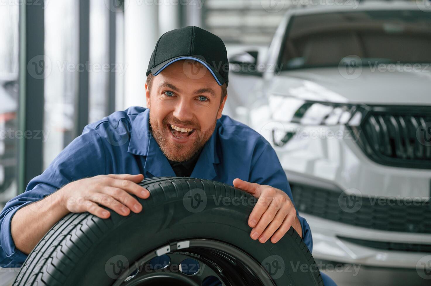 New tire. Leaning on it. Man in blue uniform, is working in the car service photo