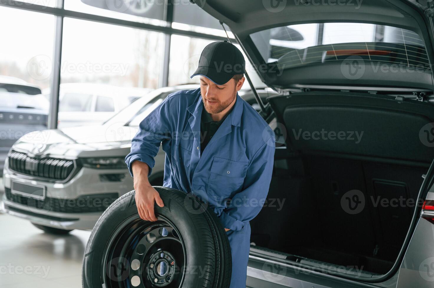 Putting the, tire out of ,automobile. Man in blue uniform is working in the car service photo