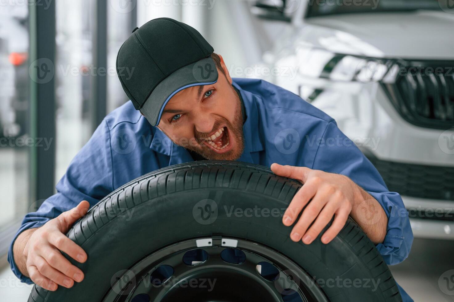 Having ,fun, smiling, with, tire. Man in blue uniform is working in the car service photo