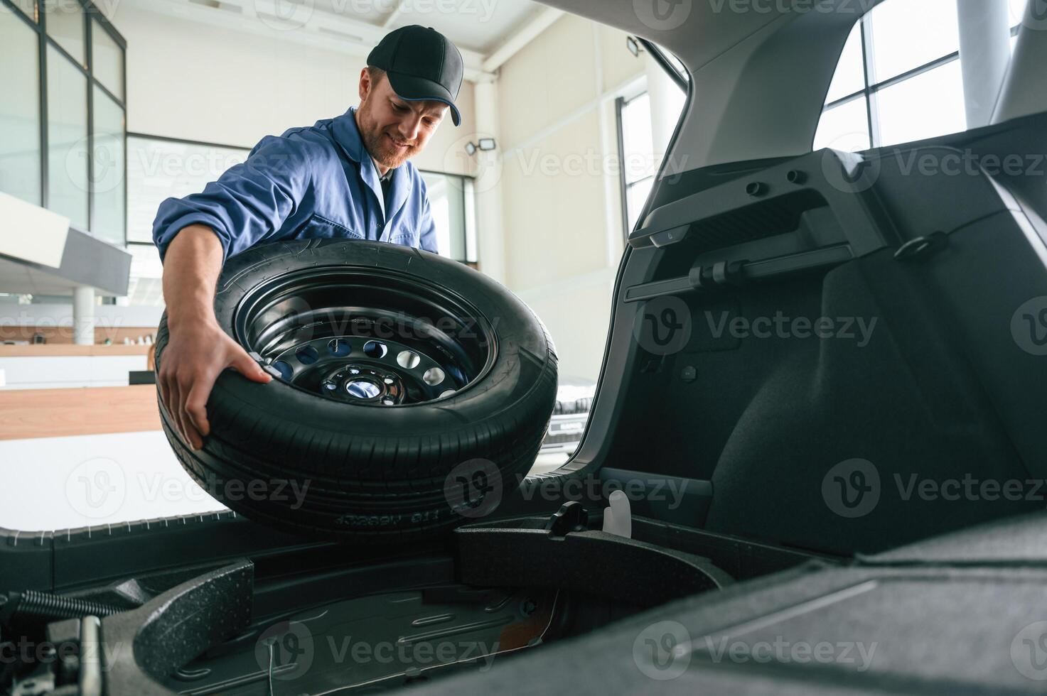 Putting the tire out of automobile... Man in blue uniform is working in the car service photo