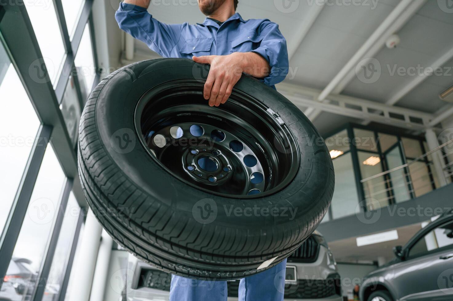 View, from, below. Holding tire. Man in blue uniform is working in the car service photo