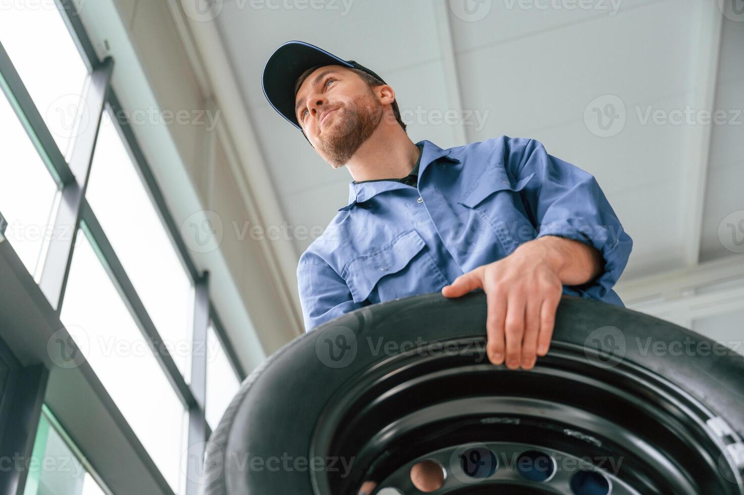 View ,from below., Holding tire. Man in blue uniform is working in the car service photo