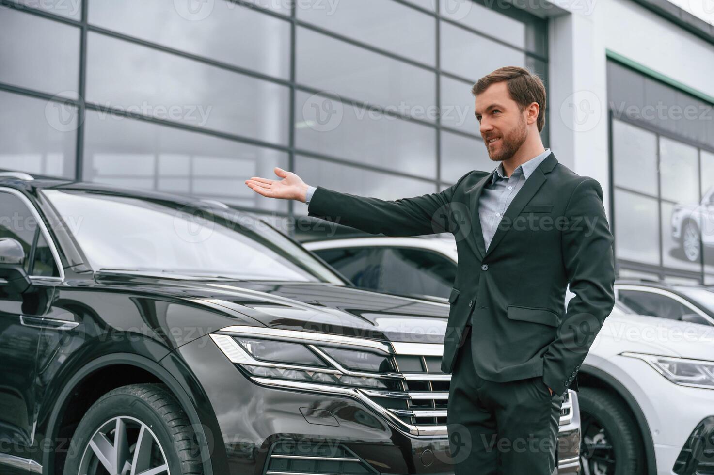 Man in black suit is outdoors near modern cars. Conception of business, selling photo