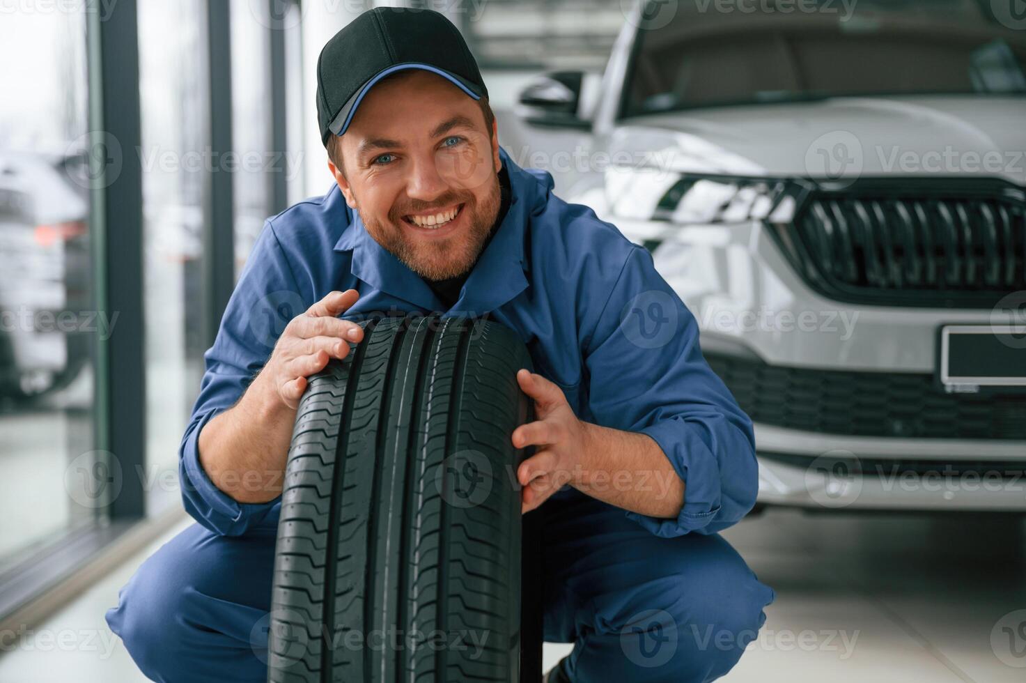 Leaning on the tire and smiling.. Man ,in ,blue uniform is working in the car service photo