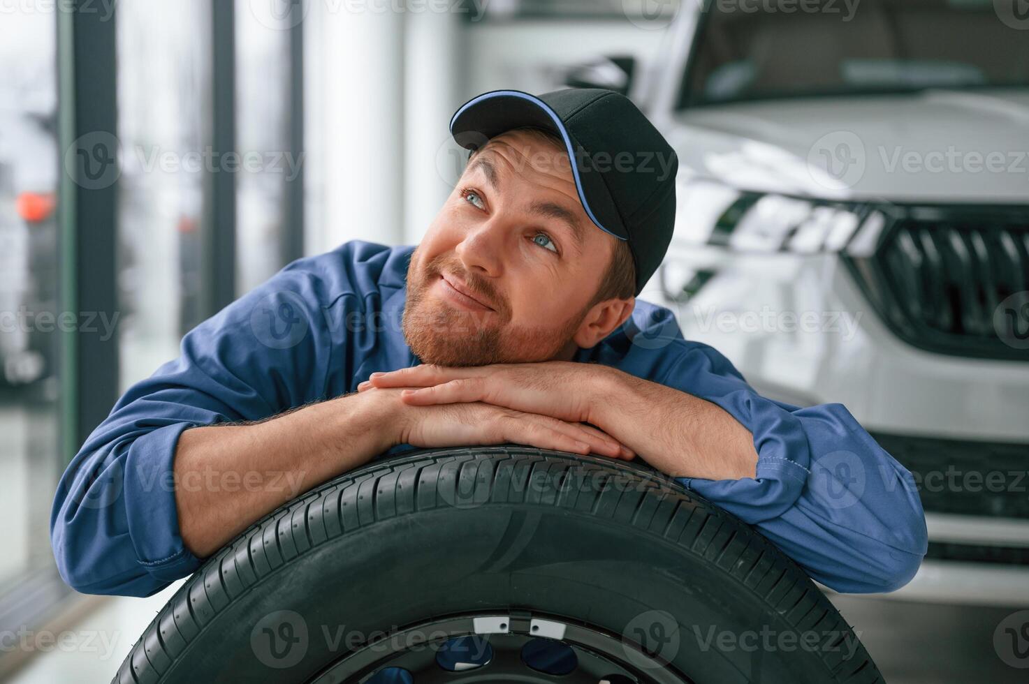 New tire. Leaning ,on it. ,Man in blue uniform is working in the car service photo