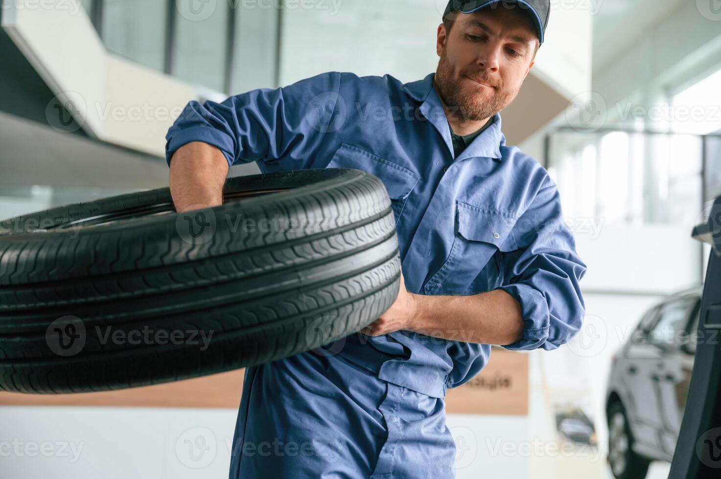 With big ,new, tire for a change. Man in blue uniform is working in the car service photo