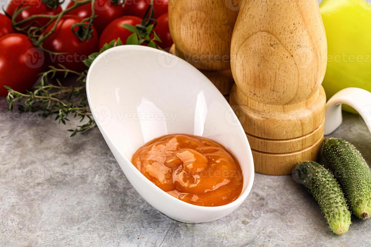 A bowl of tomato sauce next to a knife and a cucumber photo