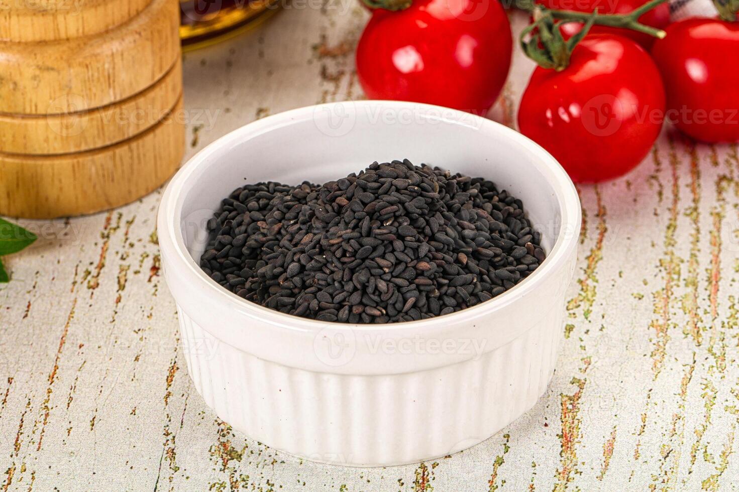 A bowl of black seeds on a table next to tomatoes and herbs photo