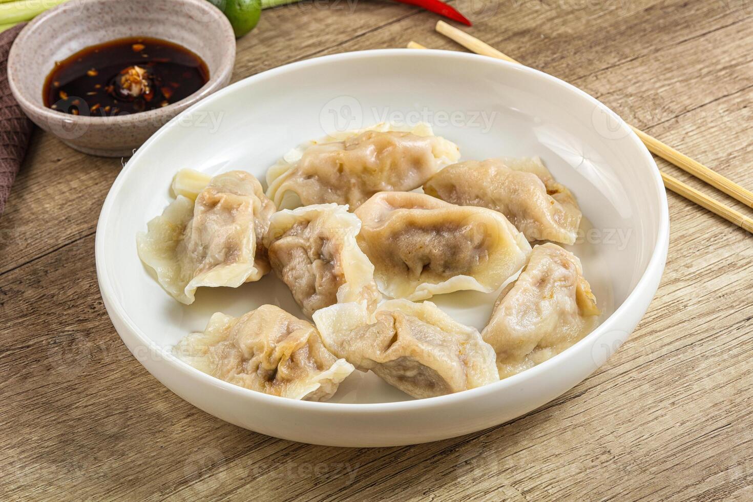 A white bowl with dumplings and chopsticks on a wooden table photo